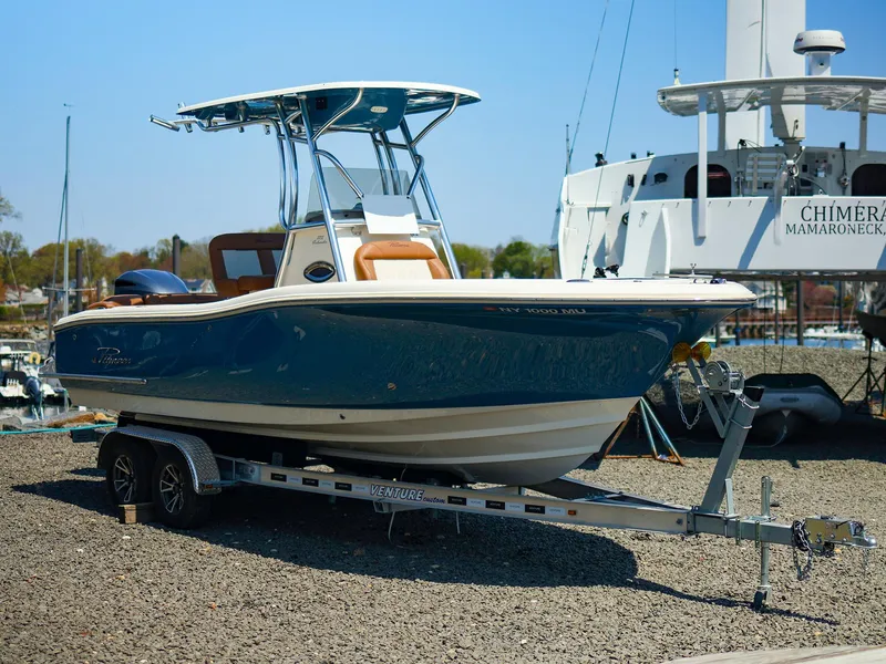 Slide: The Image of 2022 Pioneer 222 Islander boat on trailer, dockside, with blue hull and T-top. - 1