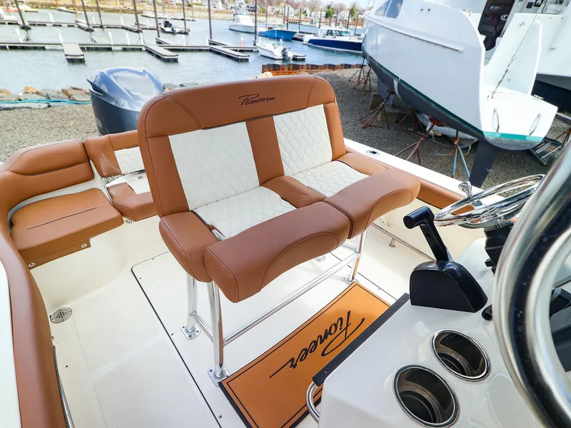 Slide: The Image of 2022 Pioneer 222 Islander boat interior with tan and white seating at marina. - 6