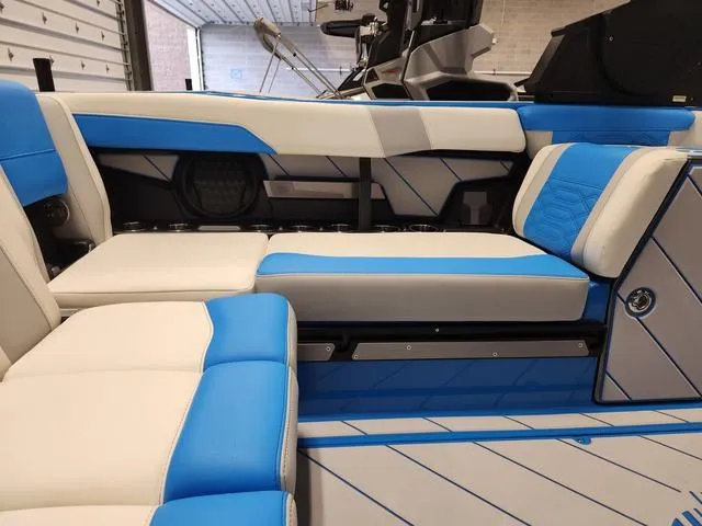 Slide: The Image of 2023 Malibu 26 LSV boat interior with blue and white seating in a garage setting. - 13
