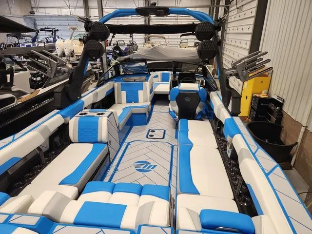 Slide: The Image of 2023 Malibu 26 LSV boat interior with blue and white seating in a showroom. - 21
