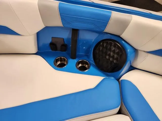 Slide: The Image of 2023 Malibu 26 LSV boat interior with blue and white seating, cup holders, and speaker. - 26