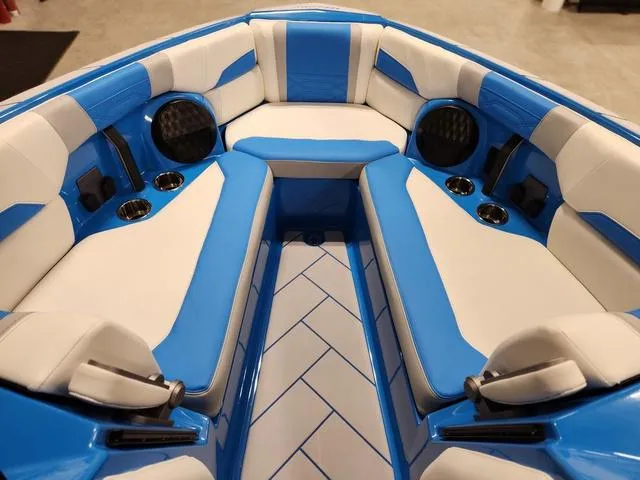 Slide: The Image of 2023 Malibu 26 LSV boat interior with blue and white seating, cup holders, and speakers. - 33