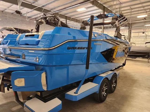 Slide: The Image of 2023 Malibu 26 LSV boat in vibrant blue on a trailer, inside a spacious warehouse. - 37