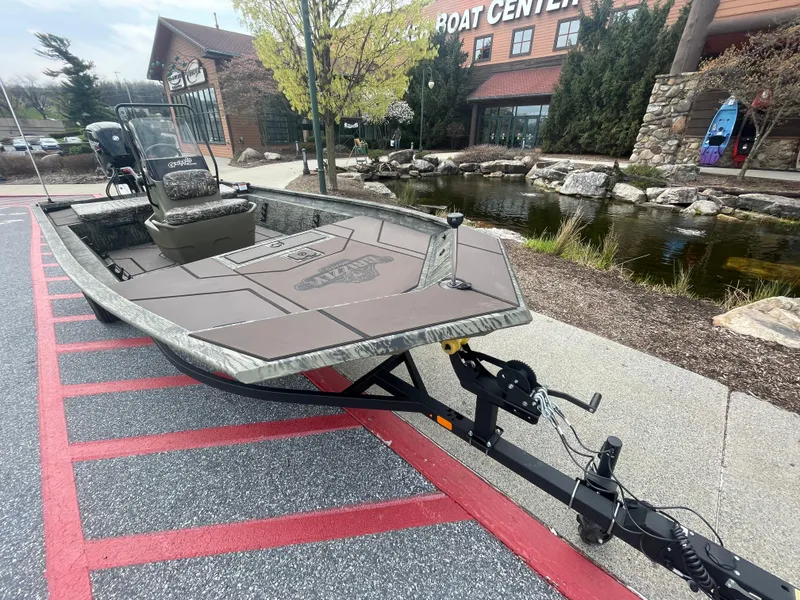Slide: The Image of 2025 Tracker Grizzly 1860 CC boat parked near a building with a pond. - 2