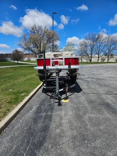 Slide: The Image of 2025 Sun Tracker Bass Buggy 16 XL Select pontoon boat on a trailer in a parking lot. - 2