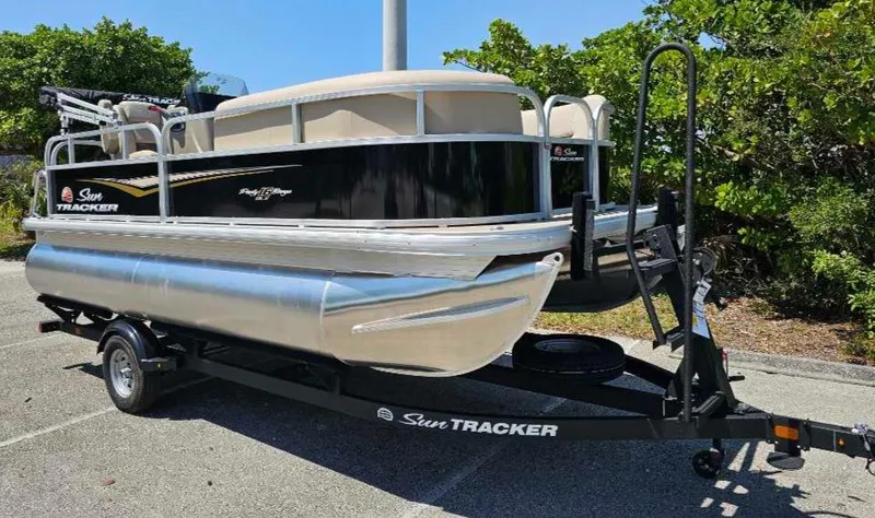 Slide: The Image of 2025 Sun Tracker Party Barge 16 DLX pontoon boat on trailer, parked outdoors. - 2