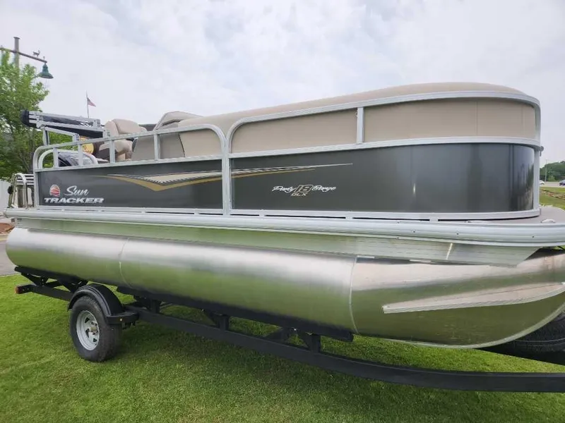 The Image of 2025 Sun Tracker Party Barge 18 DLX pontoon boat on trailer, parked on grass. - 0
