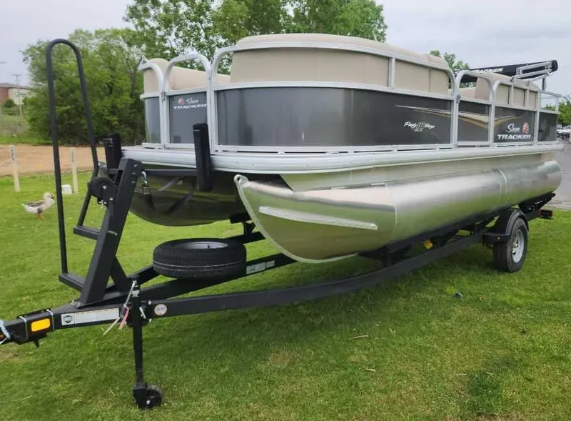 Slide: The Image of 2025 Sun Tracker Party Barge 18 DLX pontoon boat on trailer, parked on grass. - 2