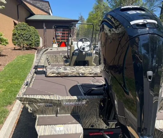 Slide: The Image of 2025 Tracker Grizzly 1860 CC boat with Mercury engine, parked outdoors. - 2