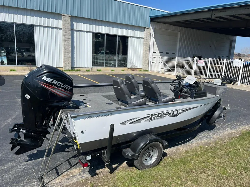 Slide: The Image of 2017 Lund 1750 Rebel XS SS boat with Mercury engine, parked outside a building. - 1
