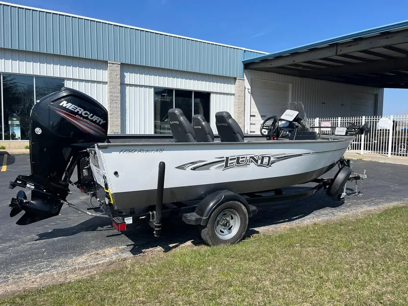 Slide: The Image of 2017 Lund 1750 Rebel XS SS boat with Mercury engine, parked outdoors near a building. - 2