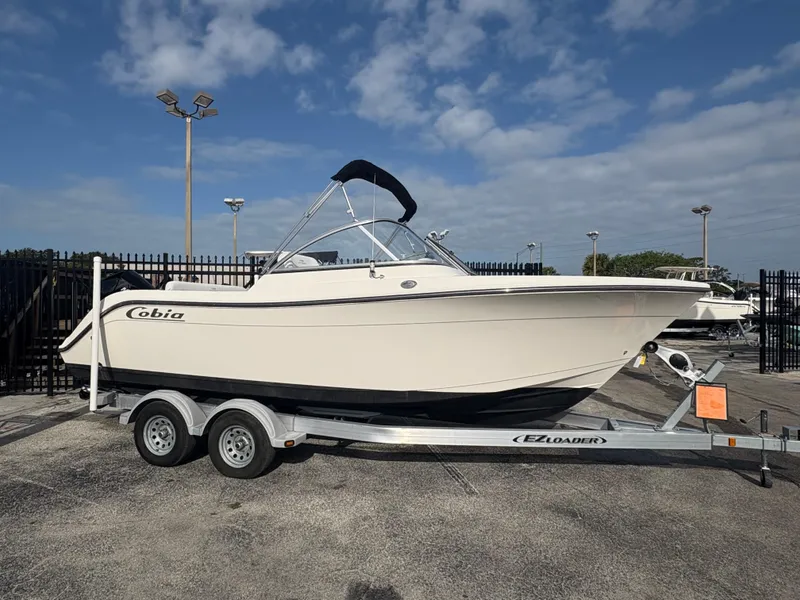 The Image of 2020 Cobia 220 Dual Console boat on trailer, parked outdoors under a partly cloudy sky. - 0