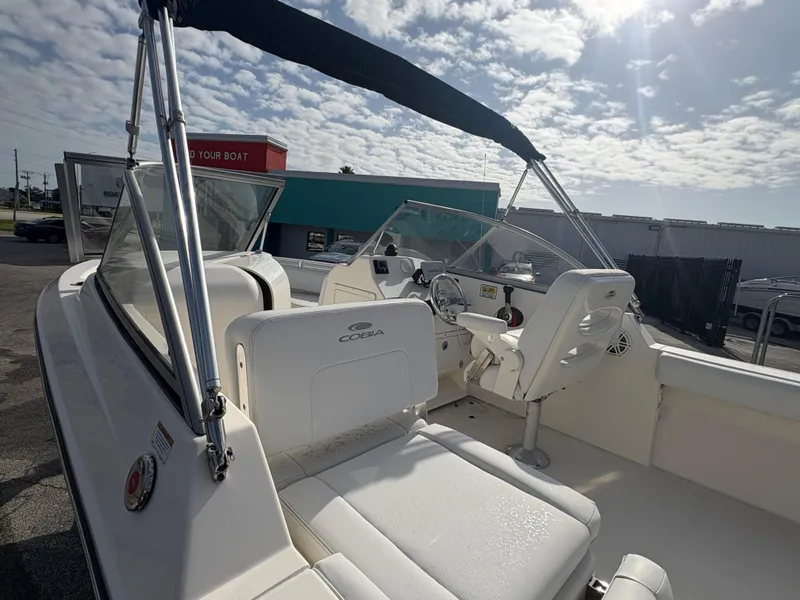 Slide: The Image of 2020 Cobia 220 Dual Console boat with seating, steering wheel, and canopy under a sunny sky. - 9