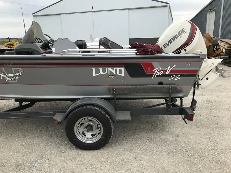 Slide: The Image of 1998 Lund 1775 Pro-V SE boat with Evinrude motor on trailer, parked outside a warehouse. - 3