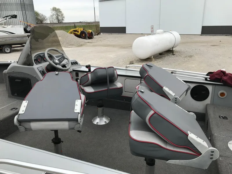 Slide: The Image of 1998 Lund 1775 Pro-V SE boat interior with gray and red seating, steering console, and outdoor setting. - 7