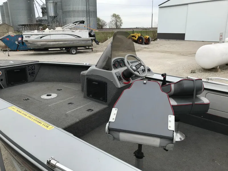 Slide: The Image of 1998 Lund 1775 Pro-V SE boat interior with steering console, parked outdoors near storage buildings. - 8