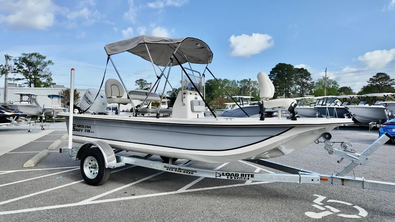 Slide: The Image of 2024 Carolina Skiff e18 JVX boat on trailer, parked outdoors under blue sky. - 3