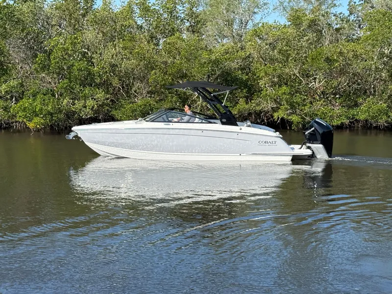 Slide: The Image of 2025 Cobalt R6 Outboard boat cruising on a calm river with lush greenery. - 2