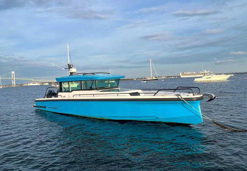 The Image of 2020 Axopar 37 XC boat in blue, anchored on calm water with a bridge in the background. - 1