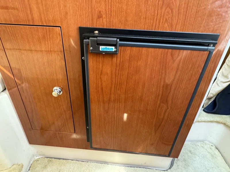 Slide: The Image of Wood-paneled interior of 2006 Regal 2565 Window Express boat with a compact fridge. - 29