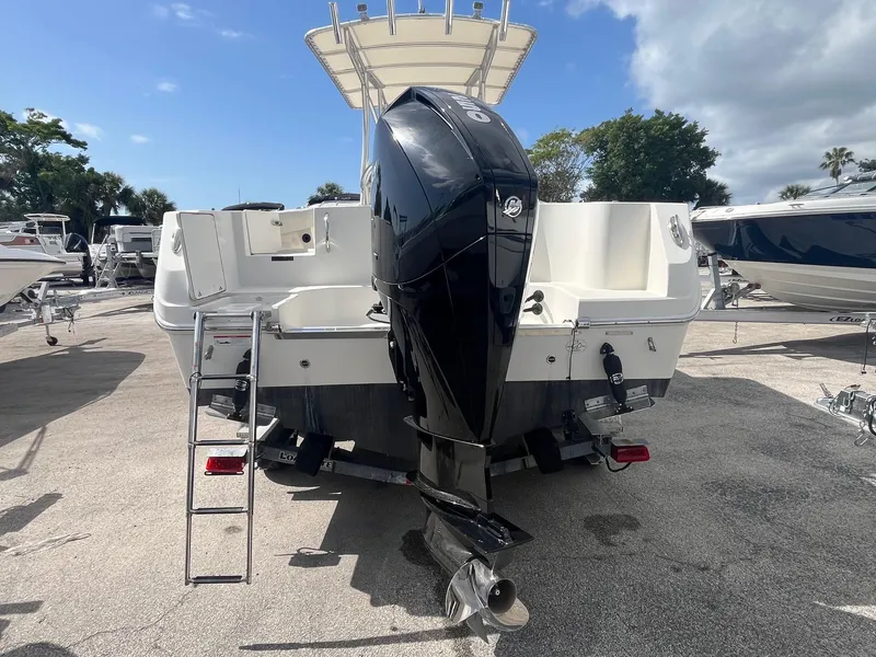 Slide: The Image of 2022 Sailfish 242 CC boat with outboard motor, ladder, and T-top, parked on pavement. - 3