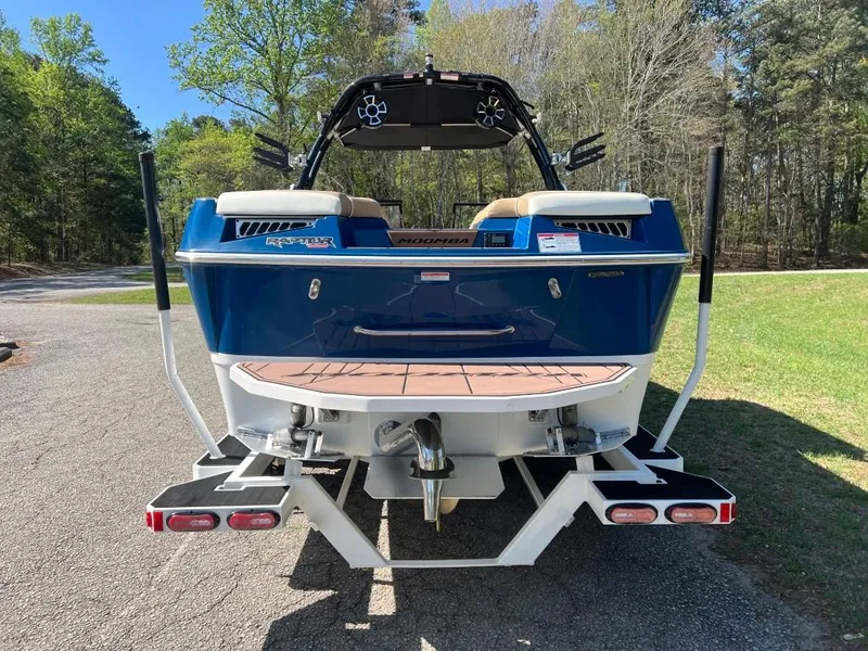 Slide: The Image of 2021 Moomba Makai boat, blue exterior, parked on a driveway with trees in the background. - 4