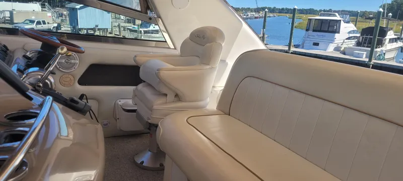 Slide: The Image of 1998 Sea Ray 450 Sundancer interior with beige seating and helm, docked by the water. - 39