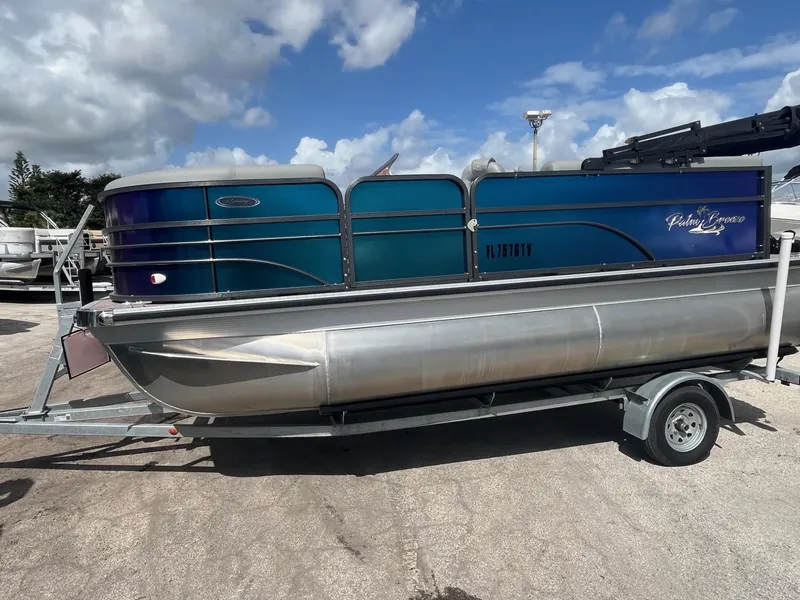Slide: The Image of 2024 Lexington 17 Emerg pontoon boat on trailer under a partly cloudy sky. - 1