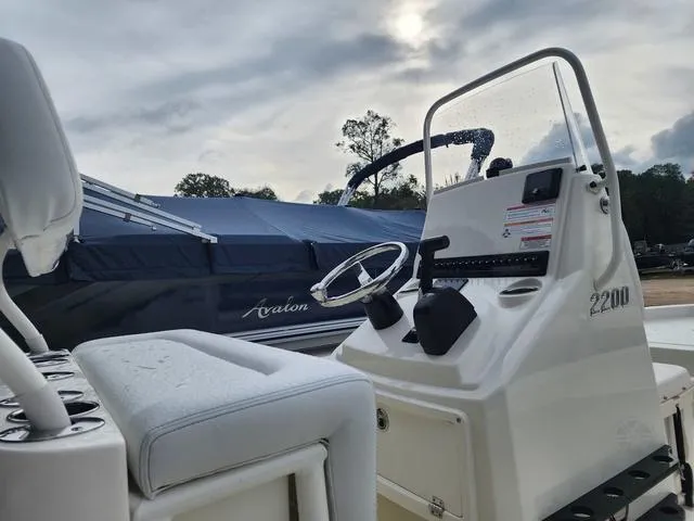 Slide: The Image of 2024 Pathfinder 2200 TRS boat console with steering wheel, docked beside a covered vessel. - 23