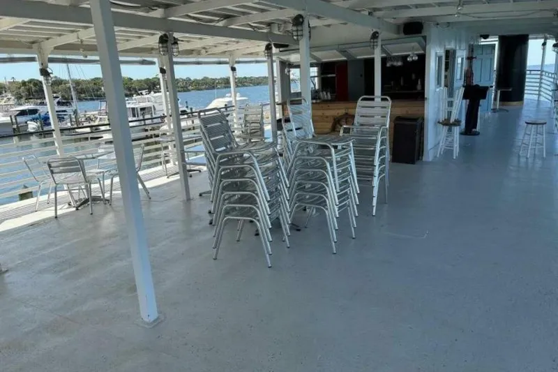 Slide: The Image of Spacious deck of 1984 custom paddle wheel boat with stacked chairs and marina view. - 12