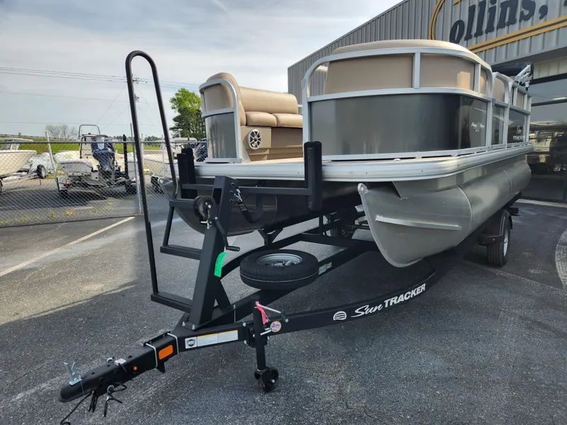 Slide: The Image of 2025 Sun Tracker Party Barge 16 DLX pontoon boat on trailer, parked outdoors. - 4