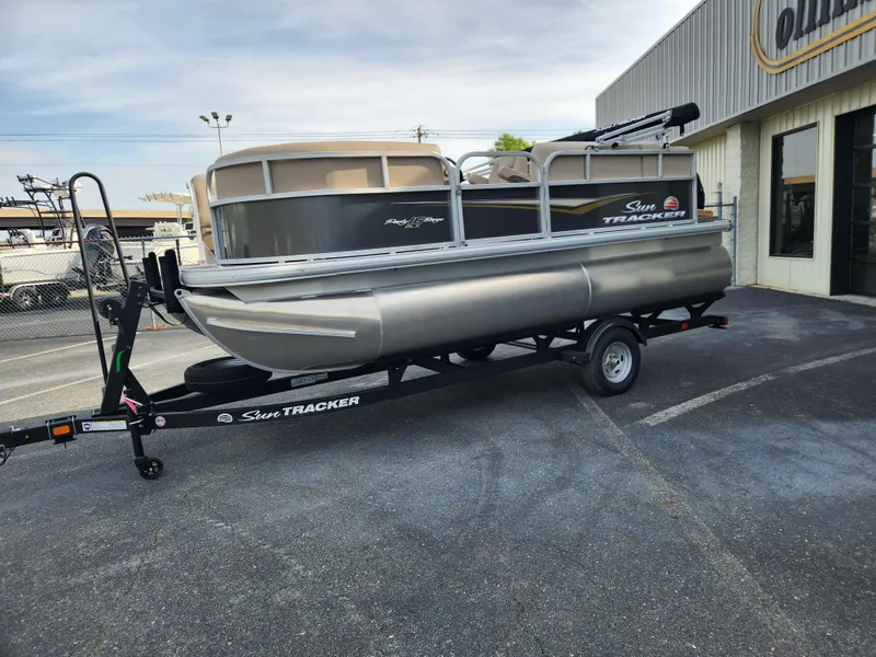 Slide: The Image of 2025 Sun Tracker Party Barge 16 DLX pontoon boat on trailer, parked outside dealership. - 5