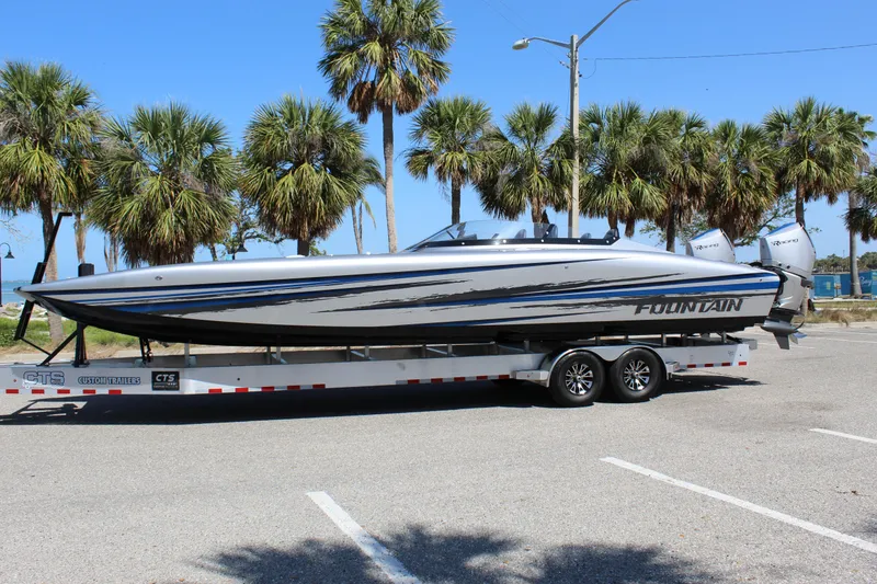 The Image of 2025 Fountain 34 Thundercat boat on trailer, parked near palm trees under clear blue sky. - 0