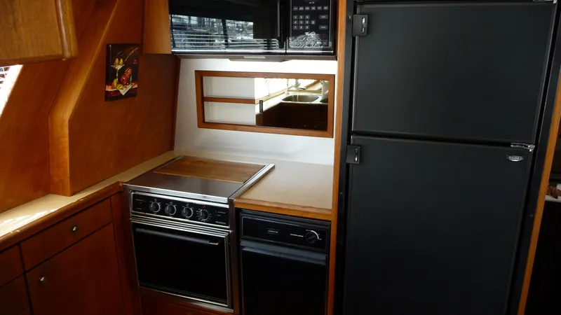 Slide: The Image of 1995 Bayliner 4788 Pilot House Motoryacht kitchen with stove, fridge, and wooden cabinetry. - 15