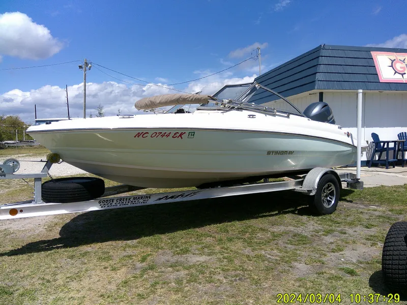 Slide: The Image of 2019 Stingray 191 Dual Console boat on trailer, parked outdoors under a partly cloudy sky. - 4
