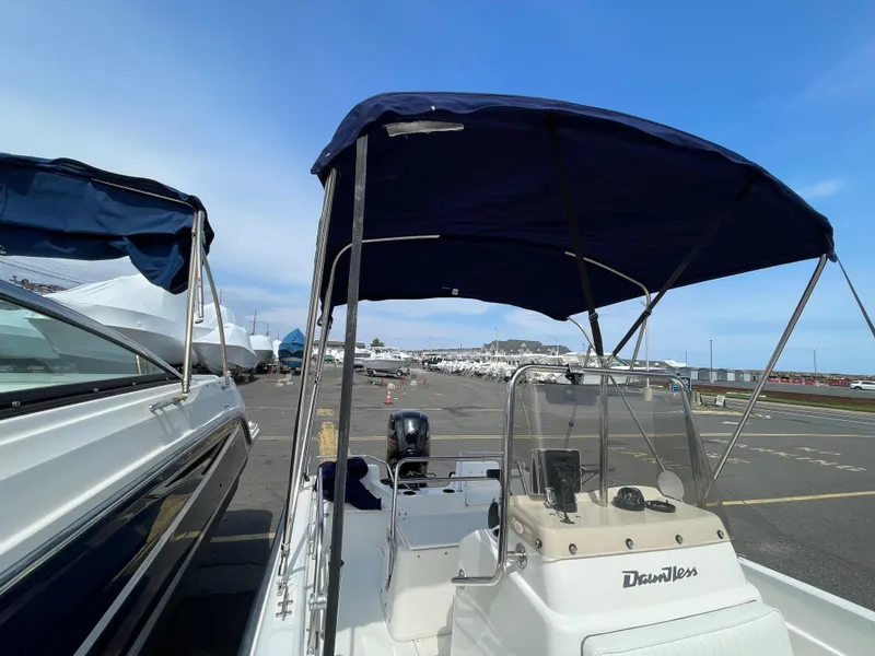 Slide: The Image of 1999 Boston Whaler 16 Dauntless boat with blue canopy in a marina setting. - 18