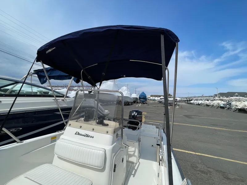 Slide: The Image of 1999 Boston Whaler 16 Dauntless boat with blue canopy in a marina setting. - 19