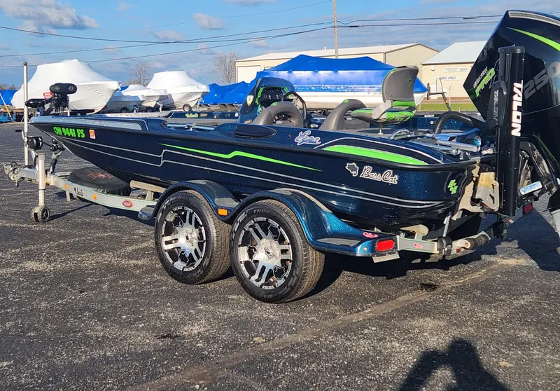 Slide: The Image of 2014 Bass Cat Eyra boat on trailer, blue with green accents, parked outdoors. - 16