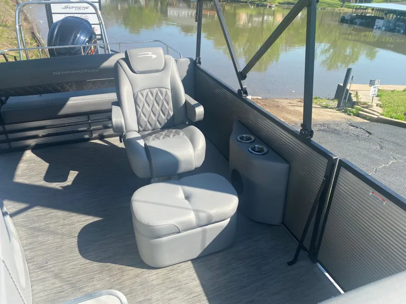 Slide: The Image of 2022 Bennington LX 24 Swingback interior with gray seating and cup holders by a lake. - 13