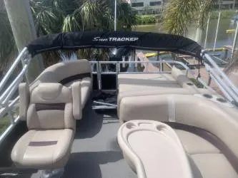 Slide: The Image of 2017 Sun Tracker Party Barge 24 DLX with beige seating and canopy, docked near palm trees. - 4