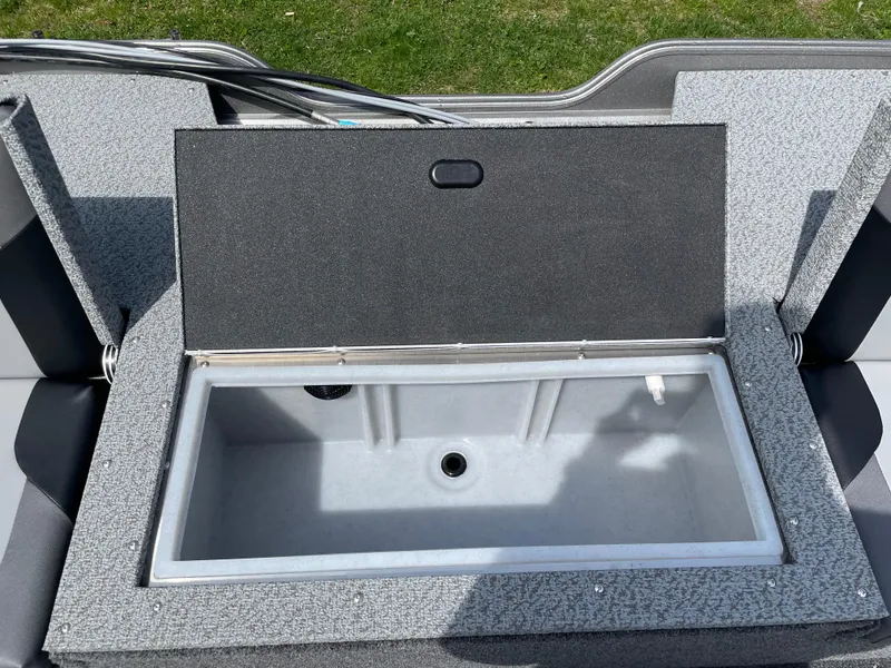 Slide: The Image of 2025 Crestliner 1750 Hawk SC livewell, open lid, gray interior, on grassy background. - 5