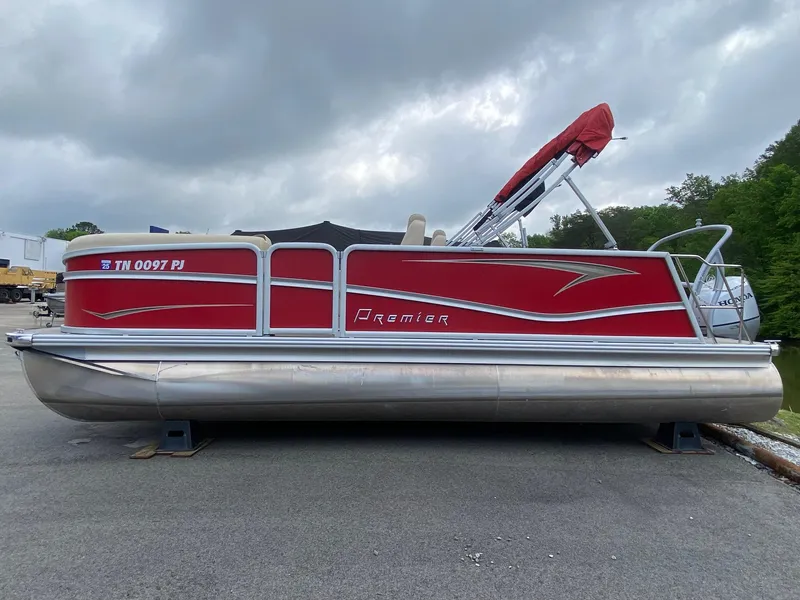 Slide: The Image of 2022 Premier 210 Sunsation RL pontoon boat with red exterior, parked on pavement. - 2