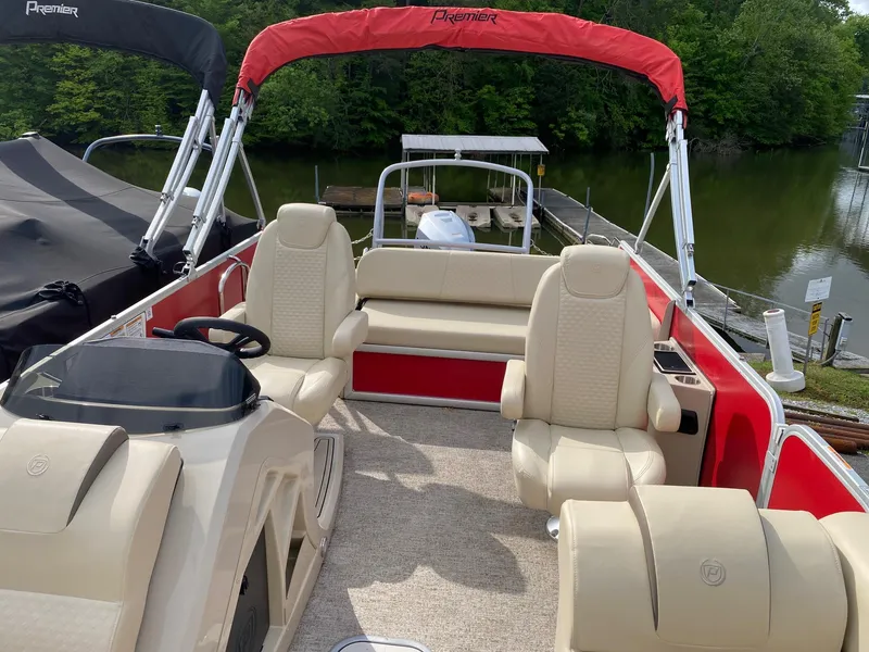 Slide: The Image of 2022 Premier 210 Sunsation RL pontoon boat with beige seating and red accents on a calm lake. - 9