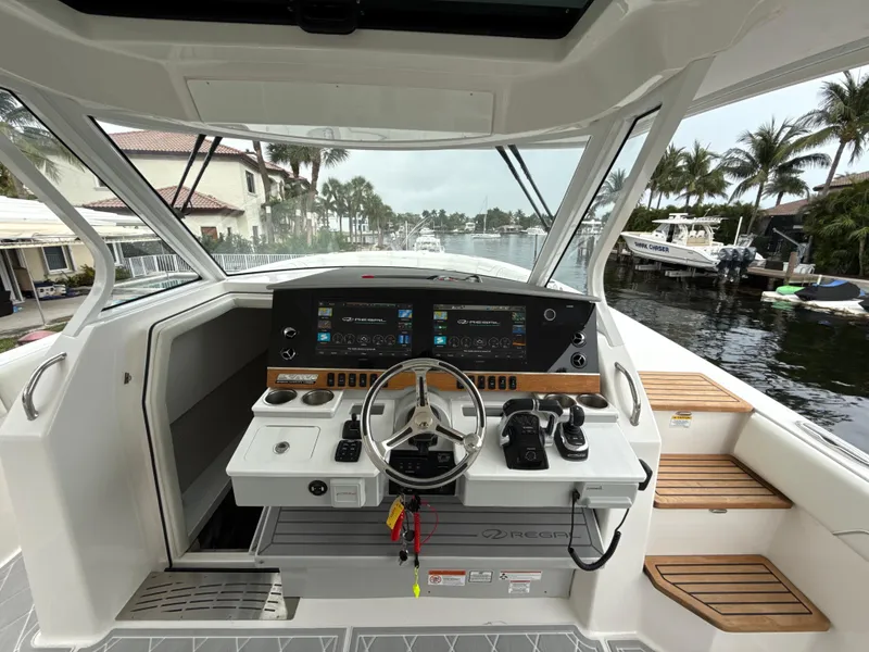 Slide: The Image of 2021 Regal 38 SAV boat helm with modern controls, docked near palm trees. - 14