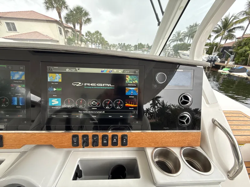 Slide: The Image of 2021 Regal 38 SAV dashboard with touchscreen display and controls, docked near palm trees. - 16