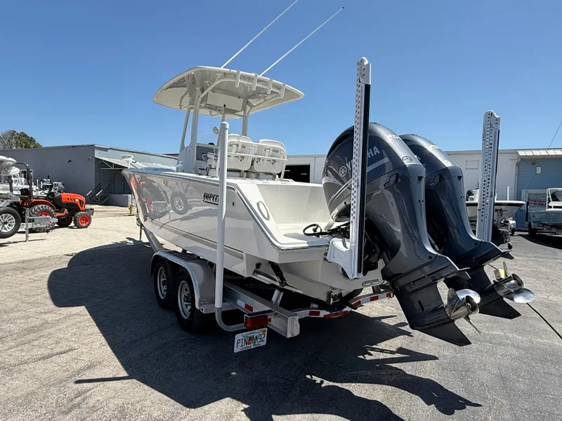 Slide: The Image of 2016 Jupiter 26 boat on trailer with dual outboard motors in a sunny industrial area. - 2