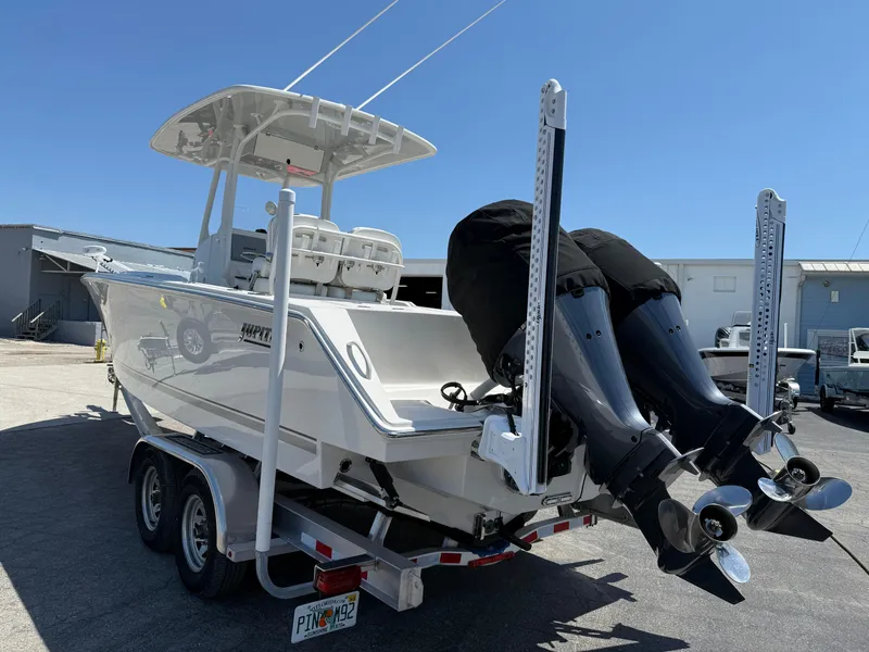 Slide: The Image of 2016 Jupiter 26 boat on trailer with dual outboard motors, parked outdoors. - 31
