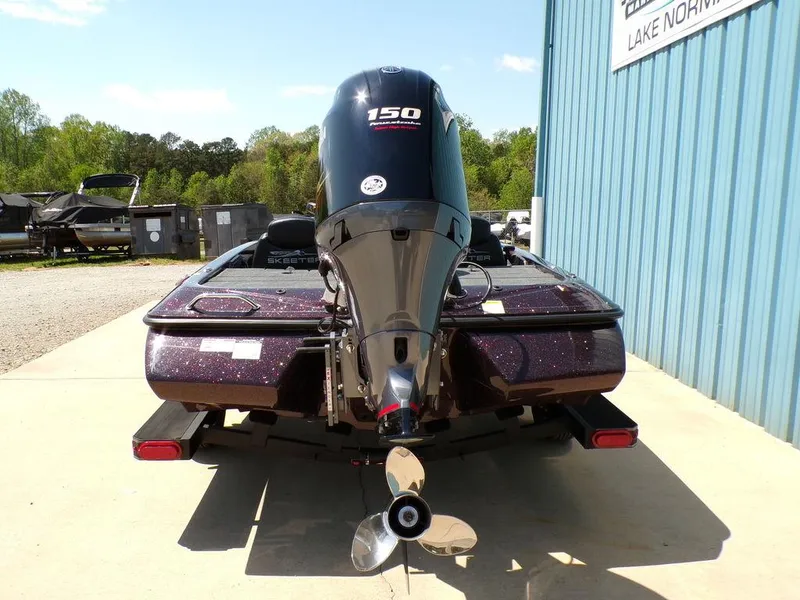 Slide: The Image of 2024 Skeeter ZX150 boat with powerful outboard motor, parked near a blue building. - 17