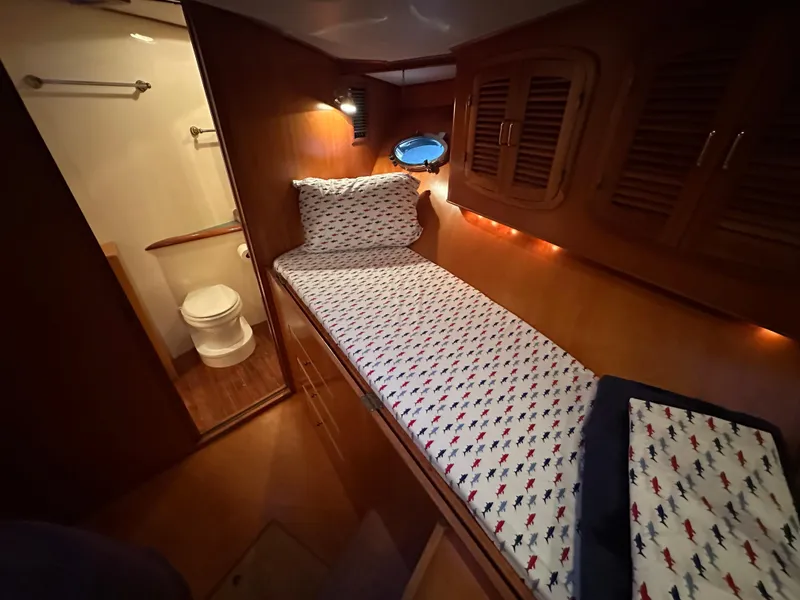Slide: The Image of 1999 Mikelson Long-Range Luxury Sportfish cabin with bed, wooden cabinets, and adjacent bathroom. - 35