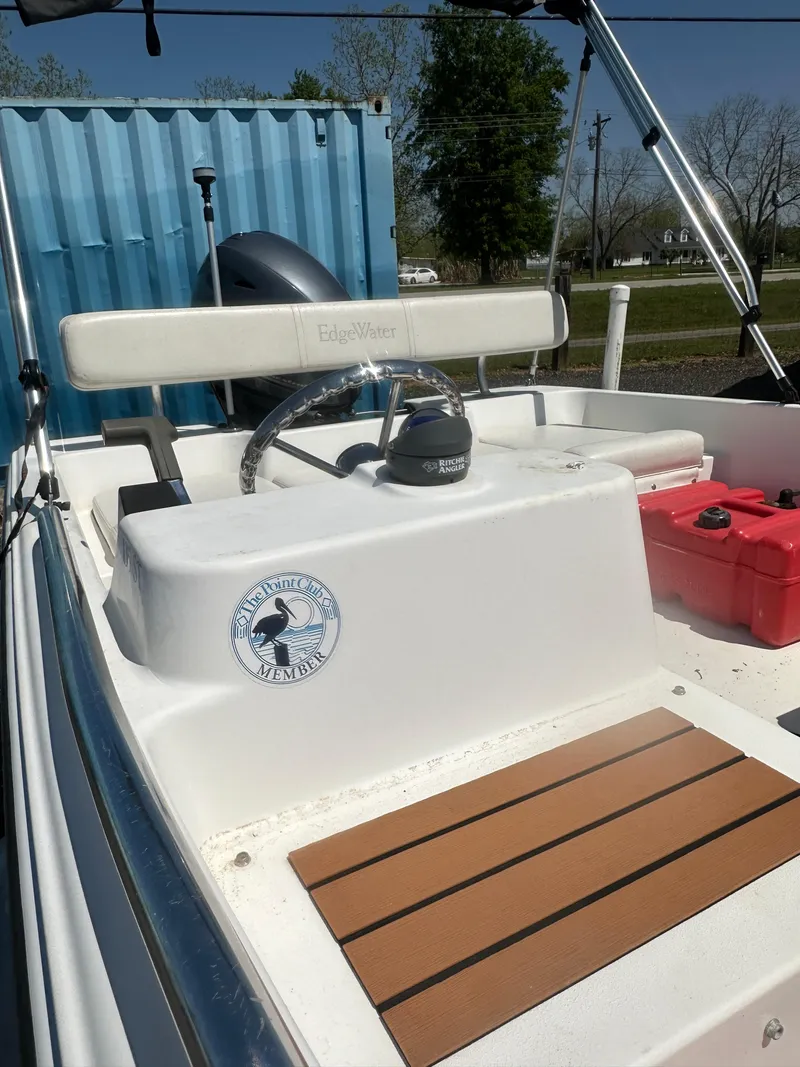 Slide: The Image of Edgewater 135ST 2002 boat interior with steering wheel and seating, docked near a blue container. - 23